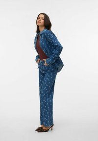 Dżinsowy strój z niebieskim kwiatowym wzorem, składający się z długiego rękawa koszuli i luźnych spodni. Brązowe szpilki dopełniają look.