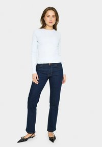 Ljust blå ribbad långärmad topp i kombination med mörkblå raka jeans. Svarta spetsiga skor med rosettdekoration kompletterar outfiten.