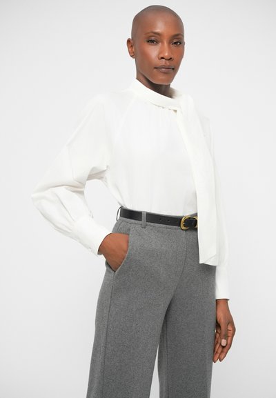 White long-sleeve blouse with a scarf detail, paired with gray tailored trousers and a black belt featuring a gold buckle.