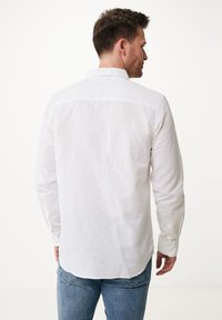 Camisa blanca de manga larga de lino, con cuello clásico, puños abotonados y dobladillo curvado, combinada con vaqueros azules.