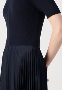 Navy dress with ribbed bodice and pleated skirt, showcasing smooth texture and a fitted top transitioning into flowing fabric.