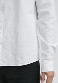 Weißes Hemd mit Knopfleiste aus leichtem Stoff, entspanntem Schnitt, langen Ärmeln und abgerundetem Saum, kombiniert mit dunklen Jeans.