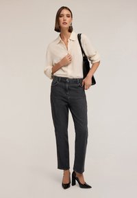 Camicia panna con maniche arrotolate, abbinata a jeans scuri con dettagli laterali. Décolleté neri e una borsa nera completano il look.