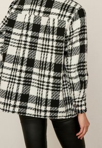 Czarna i biała marynarka w kratę, wykonana z teksturowanej tkaniny, z guzikowym mankietem i fasonem oversize, z prostym dołem.
