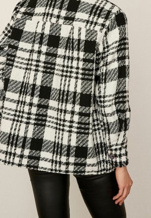 Černo-bílá kostkovaná bunda vyrobená z texturované látky, s knoflíkovým manžetovým zakončením a nadměrným střihem, se rovnou lemem.