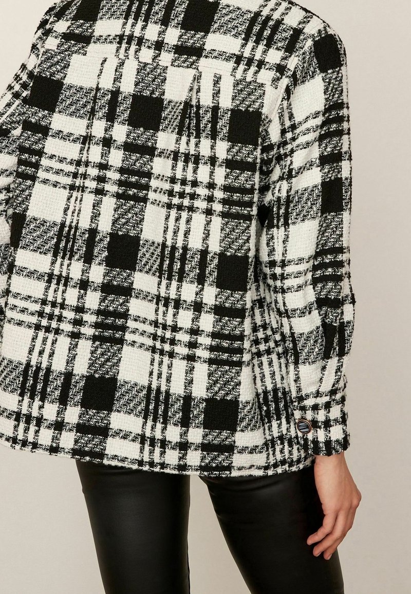 Czarna i biała marynarka w kratę, wykonana z teksturowanej tkaniny, z guzikowym mankietem i fasonem oversize, z prostym dołem.