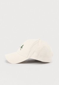 Krém színű kordbársony sapka ívelt karimával, zöld levélhímzéssel az elején és logóval az oldalon.