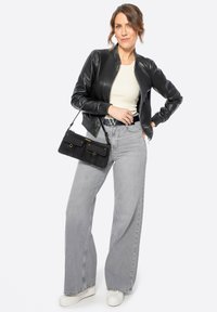 Černá kožená bomber bunda přes bílou košili, spárovaná s šedými širokými kalhotami s vysokým pasem a černou kabelkou se zlatými akcenty.