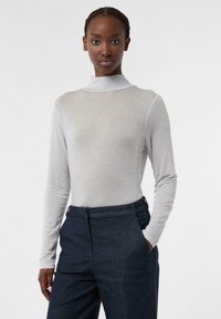 Hellgraues Langarm-Turtleneck-Oberteil mit glatter Textur, kombiniert mit dunklen Jeanshosen mit flachem Frontschnitt und Seitentaschen.
