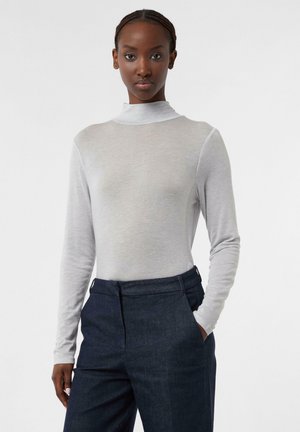 Hellgraues Langarm-Turtleneck-Oberteil mit glatter Textur, kombiniert mit dunklen Jeanshosen mit flachem Frontschnitt und Seitentaschen.