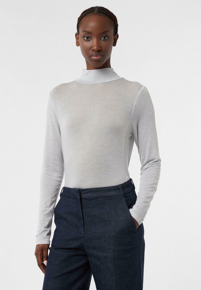 Hellgraues Langarm-Turtleneck-Oberteil mit glatter Textur, kombiniert mit dunklen Jeanshosen mit flachem Frontschnitt und Seitentaschen.