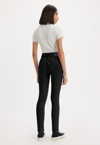 Zwarte hoge taille jeans met een strakke pasvorm en hartvormige achterzakken, gecombineerd met een textuur kort mouwtop in lichtgrijs.