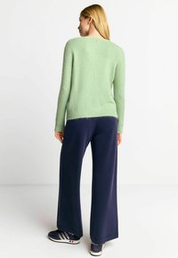 Minzgrüner Pullover aus weichem, strukturiertem Stoff; verfügt über einen runden Halsausschnitt und einen kleinen Knopf hinten. Kombiniert mit dunkelblauen weit geschnittenen Hosen.