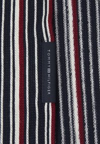 Nertinis audinys su tamsiai mėlynomis, baltomis ir raudonomis juostelėmis. Yra juodas etiketė su "TOMMY HILFIGER" baltais užrašais. Audinys su tekstūruotu raštu visame plote.