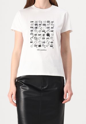 Vrouw draagt een wit T-shirt met zwarte abstracte gezichten in een raster en de tekst "Karl Lagerfeld", gecombineerd met een zwarte leren rok.