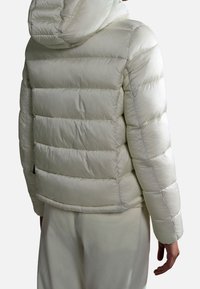 Kurtka puchowa w jasnym kremowym kolorze, z poziomymi przeszyciami, kapturem i gładką, błyszczącą teksturą. Zawiera detal w postaci kieszonki akcentującej.