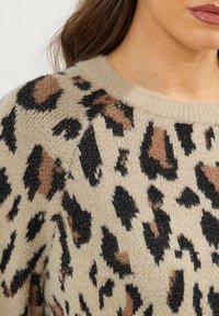 Beżowy sweter dzianinowy z nadrukiem w panterkę w czarnych i brązowych odcieniach, z okrągłym dekoltem. Miękka textura i widoczny wzór dzianiny.