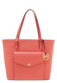 Koralfarvet lædertaske med to håndtag, forlomme, guldfarvet hardware og en præget cirkulær logo-charme. Har en struktureret form og glat tekstur.