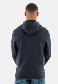 Sudadera azul marino hecha de un material de mezcla de algodón, que presenta una capucha con cordón, puños acanalados y un diseño ajustado. Detalles de costura visibles.
