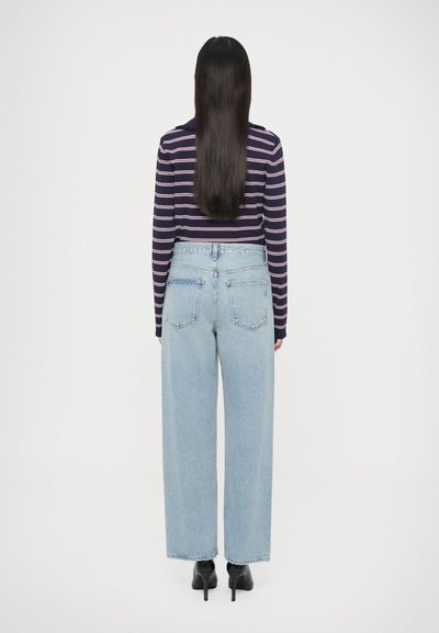 Jasnoniebieskie jeansy o szerokich nogawkach, z wysokim stanem, tylnymi kieszeniami i surowym wykończeniem na dole. Modelka ma na sobie granatowy, paskowany top z długim rękawem oraz czarne szpilki.