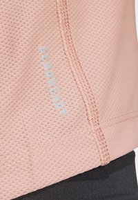 Lichtroze sporttop gemaakt van ademend meshmateriaal, met een gestructureerd oppervlak en een subtiele blauwe logo-detail.