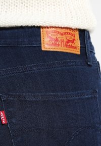 Donkerblauwe denim jeans met een leren label met rode afbeeldingen. Voorzien van een klein rood Levi's-logo op de zak.
