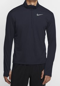 Maglione sportivo azzurro scuro a maniche lunghe con zip a quarto, realizzato in un tessuto testurizzato, con un logo Nike grigio sul lato sinistro del petto.