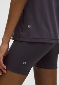 Pantaloni scurți sport de culoare gri închis și un top ajustat, ambele fabricat dintr-un material neted și elastic. Fiecare articol prezintă un logo pe partea stângă.
