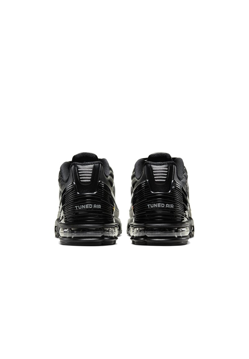 Zapatillas deportivas negras con parte superior texturizada, acolchado de aire visible y la marca "TUNED AIR" en el talón. Diseño elegante y moderno.
