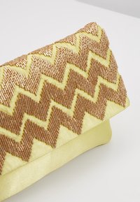 Kabelka přes rameno v žlutém saténu se zigzagovým vzorem v zlatých a bronzových korálcích s trojúhelníkovým uzávěrem. Celkově hladká textura.