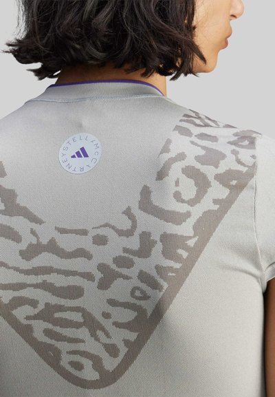 Harmaa urheilupaita, jossa on suuri ruskea abstrakti leopardikuvio takana ja pyöreä Adidas-logo kauluksen lähellä.