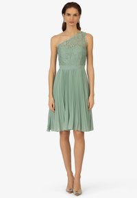 Robe mint green à une épaule avec un corsage en dentelle délicate, une jupe plissée et une taille cintrée. Complétée par des talons brillants et ornés.