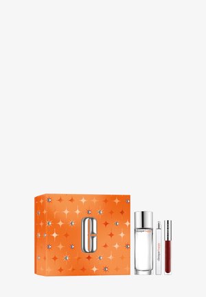 Coffret de cadeaux Clinique avec une boîte orange à motifs d'étoiles, contenant un flacon de parfum en verre, un spray de voyage et un produit à lèvres rouge.