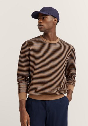 Braun gestreifter Pullover aus strukturiertem Stoff, Rundhalsausschnitt und gerippte Bündchen. Kombiniert mit marineblauen Hosen und einer dunklen Mütze.