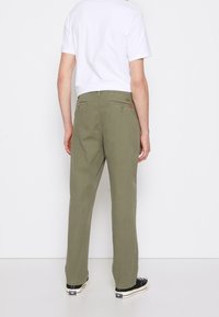 Olivgröna bomullsbukser i rak snitt, med fram- och bakfickor samt midjeband. Kombinerad med svarta skor och en vit T-shirt.