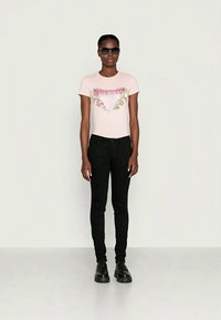 T-shirt ajustado rosa claro com estampa floral e texto, combinado com jeans skinny pretos e sapatos chunky pretos. Modelo a usar óculos de sol.