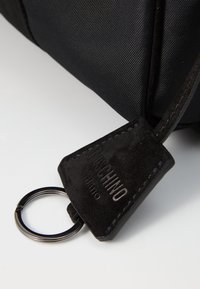 Sort nylon taske med et struktureret sort ruskindsmærke. Mærket har en præget logo og en sølvfarvet metalnøglering.