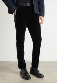 Tamsiai mėlyni sametiniai kelnės su šiuo metu populiariu slim fit, raukšlėto priekyje ir šoninėmis juostelėmis. Suderinta su juodais odiniais batais, suteikiančiais formalią išvaizdą.