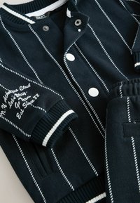 Marine gestreept gebreid tenue met een cardigan met witte knopen en accenten, geribbelde manchetten en bijpassende broek met een elastische tailleband.