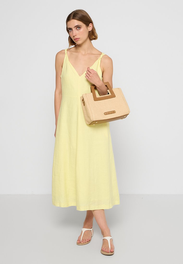 Lichtgele linnen jurk met een V-hals, gecombineerd met een beige textuur tas met een vierkante handgreep en tan accenten. Eenvoudige witte sandaaltjes.