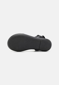 Black shoe sole with a textured surface, featuring a rounded shape and a flat heel. Smooth edge and slightly raised heel section.
