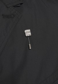 Svart tyg med sömdekoration har en silvermetallnål med en säkerhetsnålform, som ger en funktionell accent.