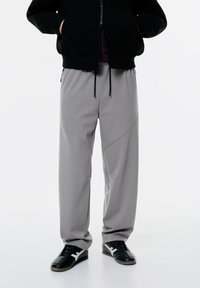 Lys grå sweatpants med en afslappet pasform, der har syede sømme, en elastisk talje og sidelommer. Bæres med sorte sneakers.