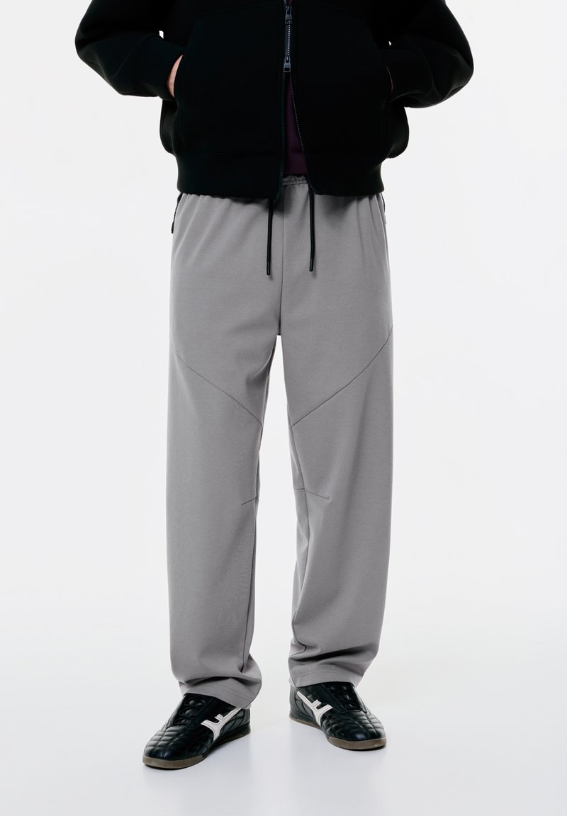 Lys grå sweatpants med en afslappet pasform, der har syede sømme, en elastisk talje og sidelommer. Bæres med sorte sneakers.