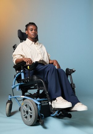 Elektrooniline ratastool musta istmega, sinise raami ja suurte hallide ratastega. Kasutaja kannab triibulist beež t-särki ja tumedaid pükse koos valgete tossudega.