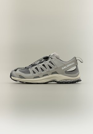 Ανοιχτό γκρι παπούτσι Salomon για trail running με πλέγμα, σύστημα γρήγορου δέσιμου και ανθεκτική μαύρη σόλα, εμφανίζεται προφίλ σε ουδέτερο φόντο.