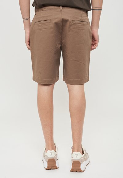 Pantaloni corti in cotone marrone con fondo dritto e due tasche posteriori, abbinati a scarpe da ginnastica beige con dettagli in bianco e texture.