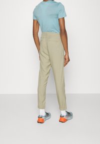 Lätta, beige byxor med en välvd passform, med en mjuk textur och bakfickor, i kombination med grå och orange sportskor.