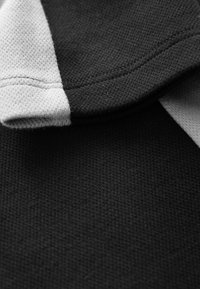 Schwarzer und grauer strukturierter Stoff mit einem dreifarbigen Design, das einen umgeschlagenen Kragen und kontrastierende Strickmuster aufweist.