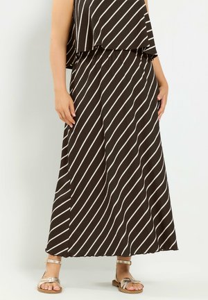 Vrouw draagt een zwart-wit diagonaal gestreepte maxi-rok en bijpassende top, gecombineerd met metallic platte sandalen met enkelriem.